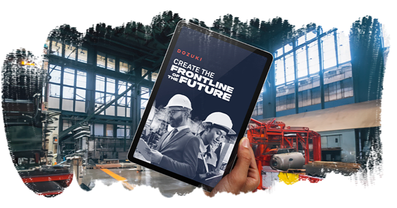 A person holds a tablet in a large industrial factory. The tablet screen displays an image of two workers wearing hard hats and the text: 