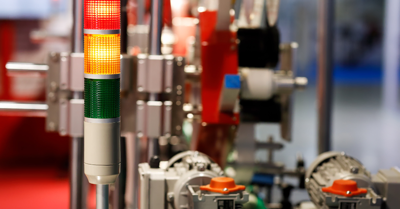 A stack light with red, yellow, and green indications is mounted on industrial machinery. The background is filled with various mechanical and electronic components, all contributing to an automated manufacturing setup. The focus is on the illuminated light.