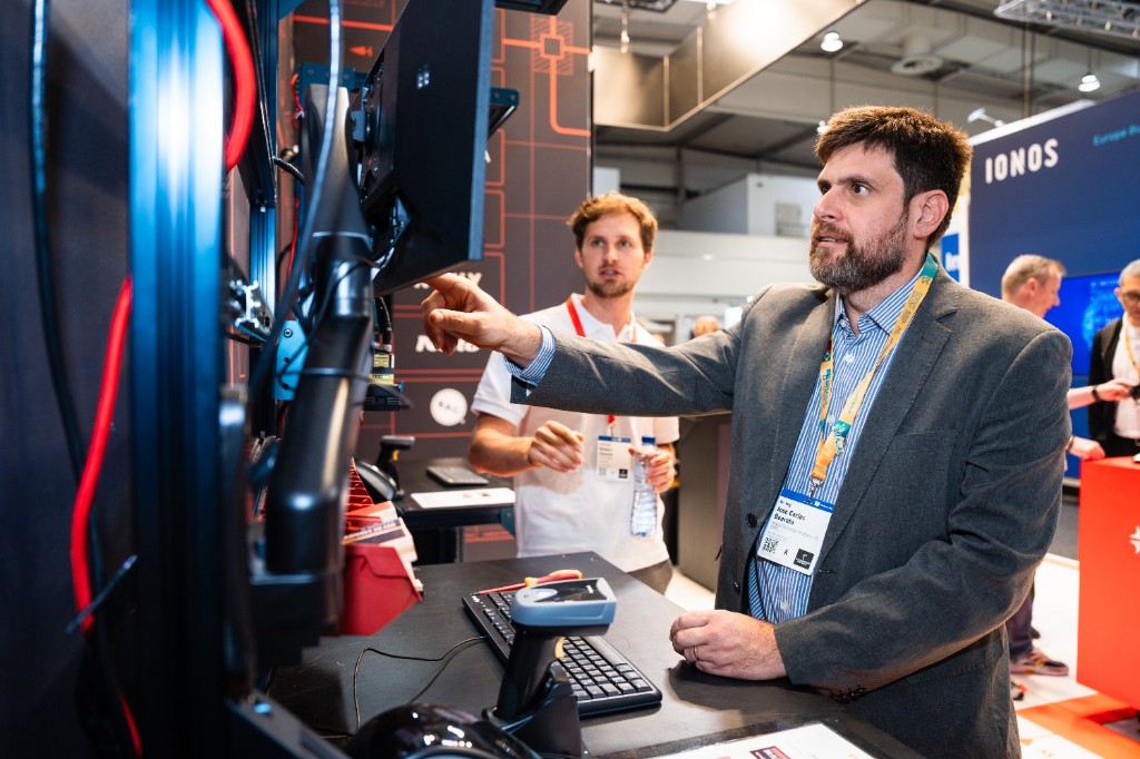 An Azumuta team member walking a visitor through the live operational dashboard on screen at Hannover Messe 2026.