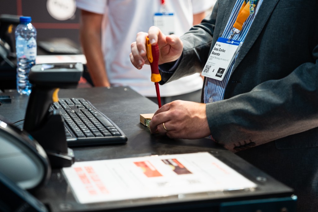 A trade show visitor using a screwdriver to assemble a beer bottle opener, guided step by step by digital work instructions at the Azumuta stand.