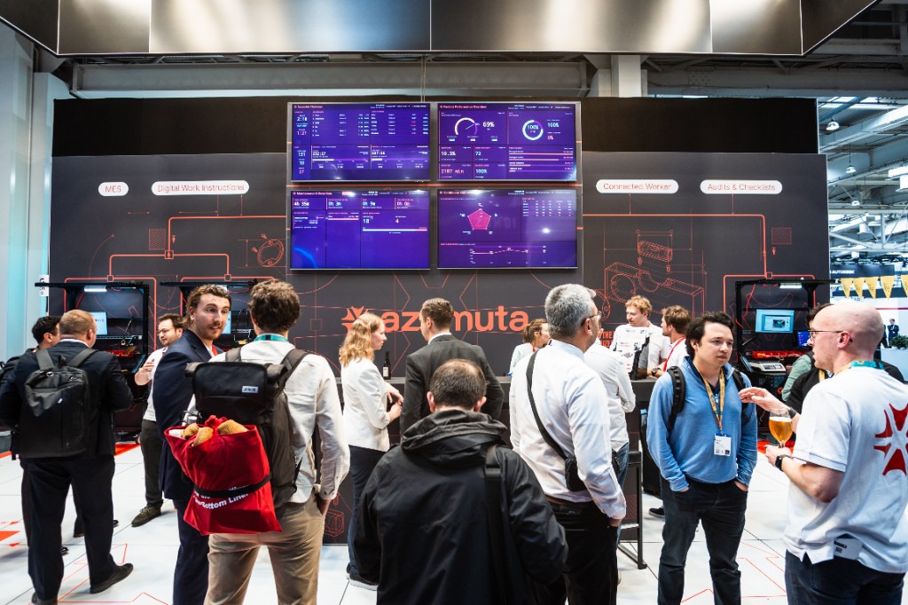 A packed Azumuta stand at Hannover Messe 2026, with visitors gathered around live dashboards on a wall of screens.