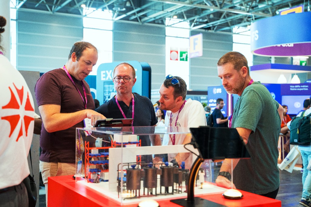 Visitors gathered around a miniature production line demo at the Azumuta stand during Tech For Industry Show in Paris.